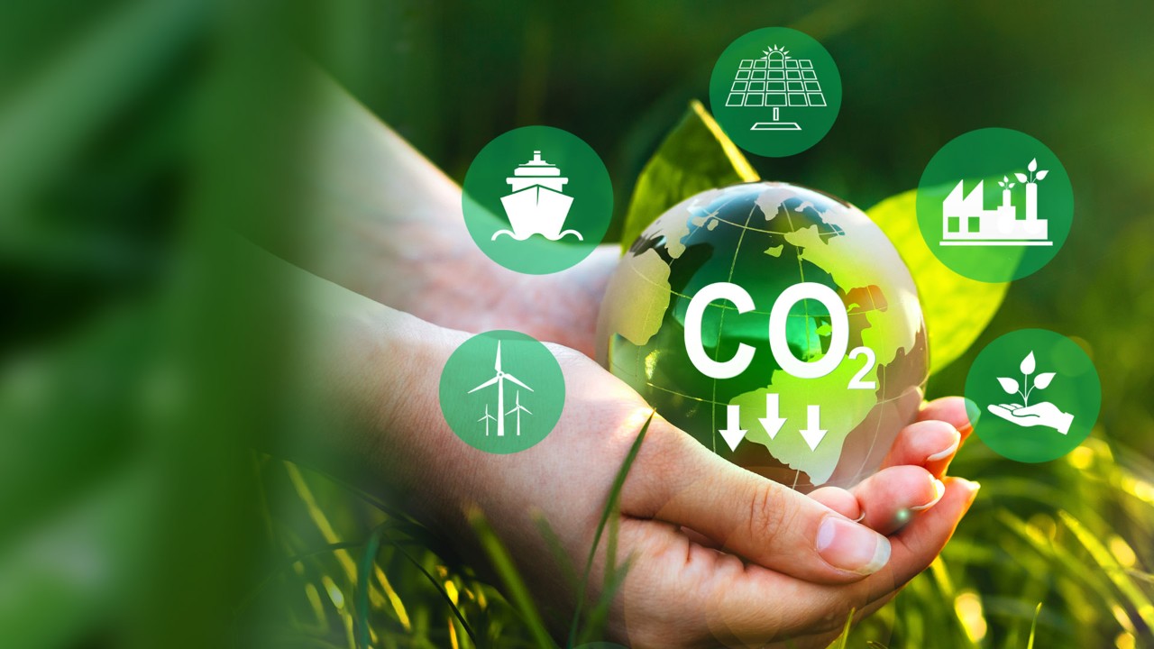 Hands holding a globe with carbon reduction and renewable energy symbols